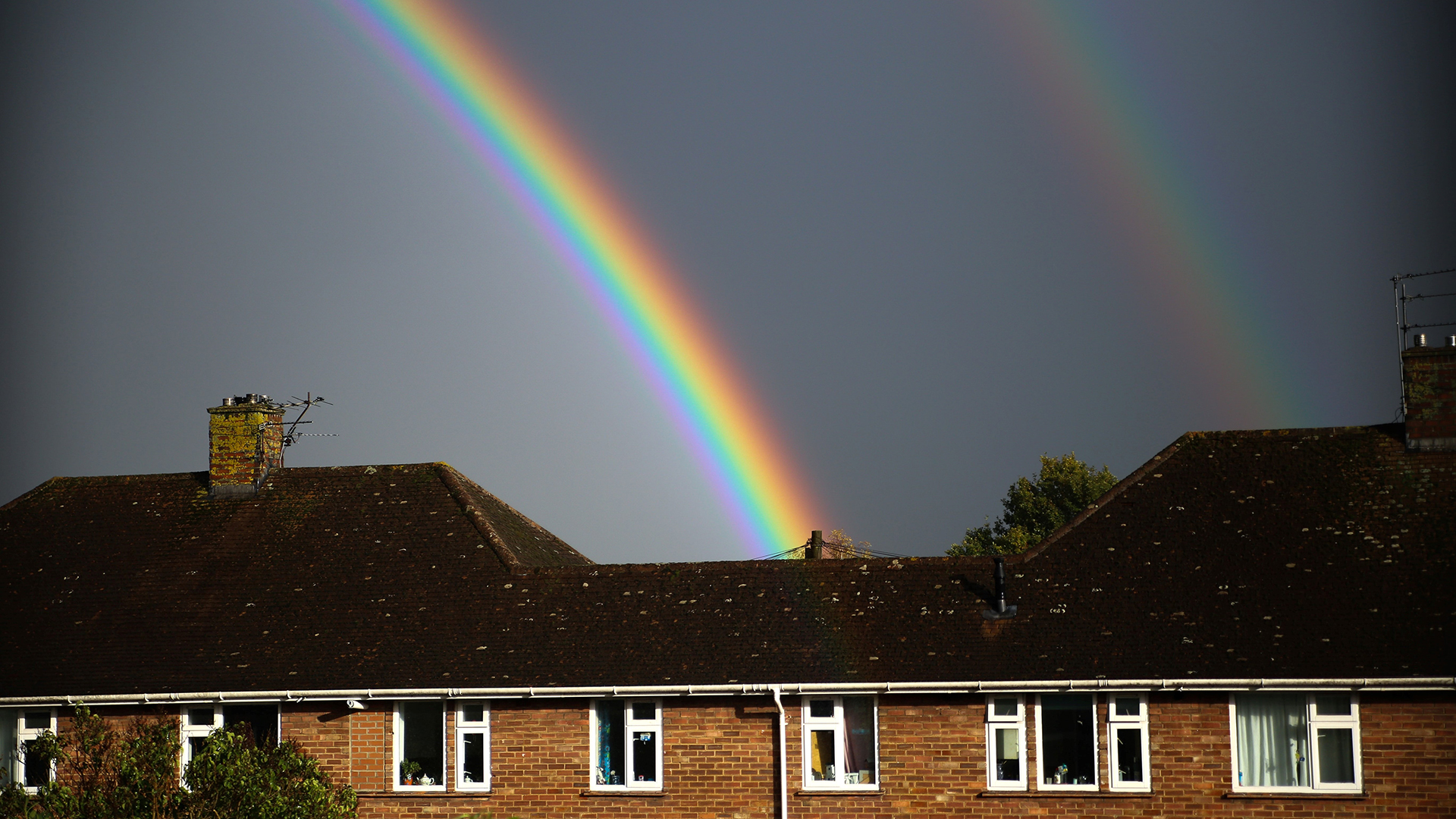 Double rainbow appearing over roofs of houses